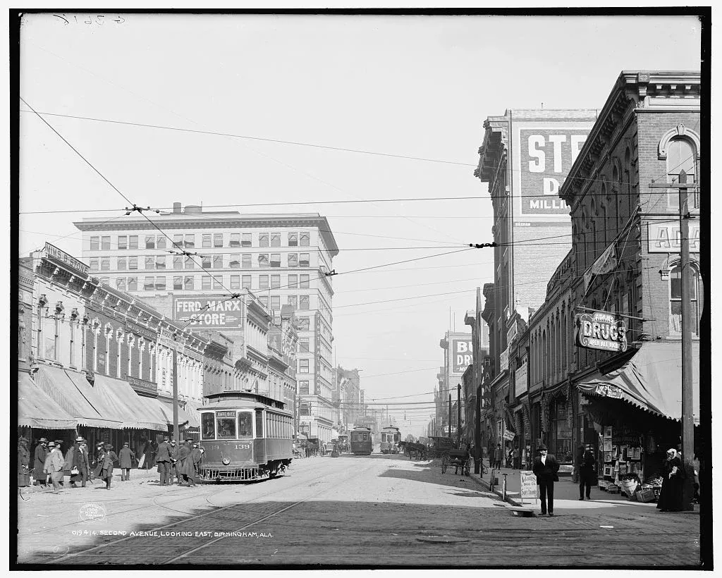 Black and white photograph of streetcars, pedestrians, shopfronts and overhead wires along Second Avenue in Birmingham, Alabama.
