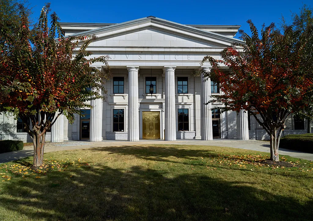 Columned entrance of the Arkansas Supreme Court building, framed by trees with autumn leaves.