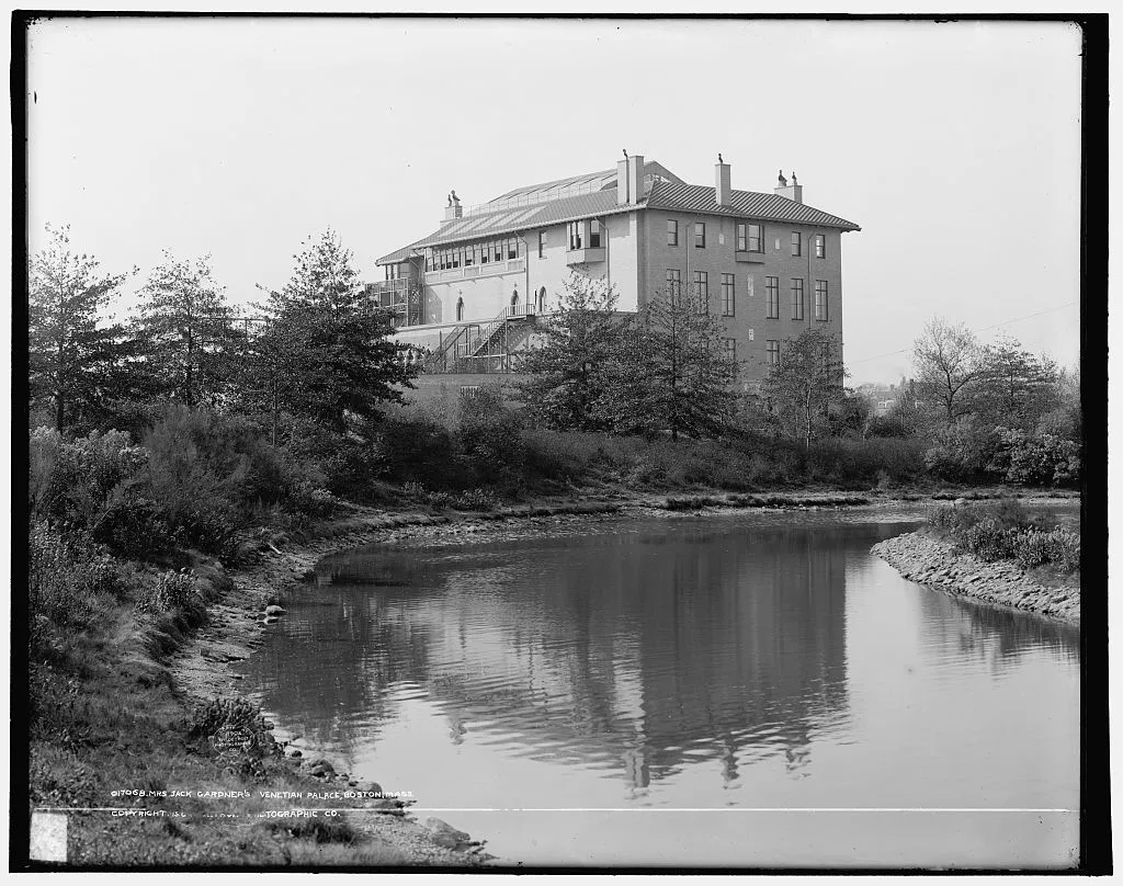 A black-and-white 1904 view of the Gardner Museum above a wooded bank and reflective water.
