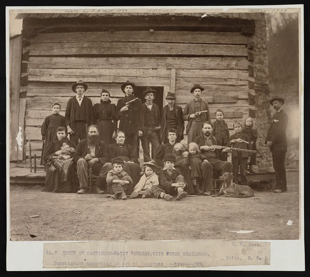 An 1899 posed portrait of Hatfield family members outside a cabin, with several adults holding firearms.