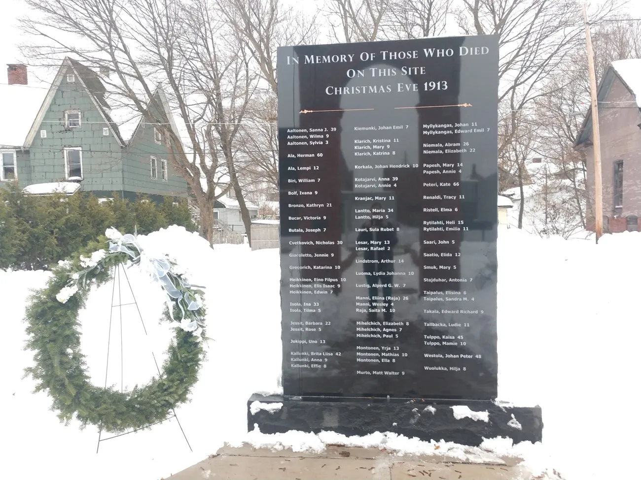 A dark granite memorial in the snow lists the names and ages of those who died at Italian Hall on Christmas Eve 1913.
