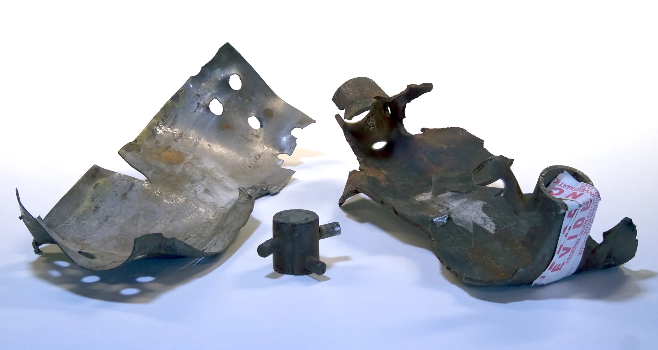 Three metal bomb fragments against a pale background, with evidence labels attached.