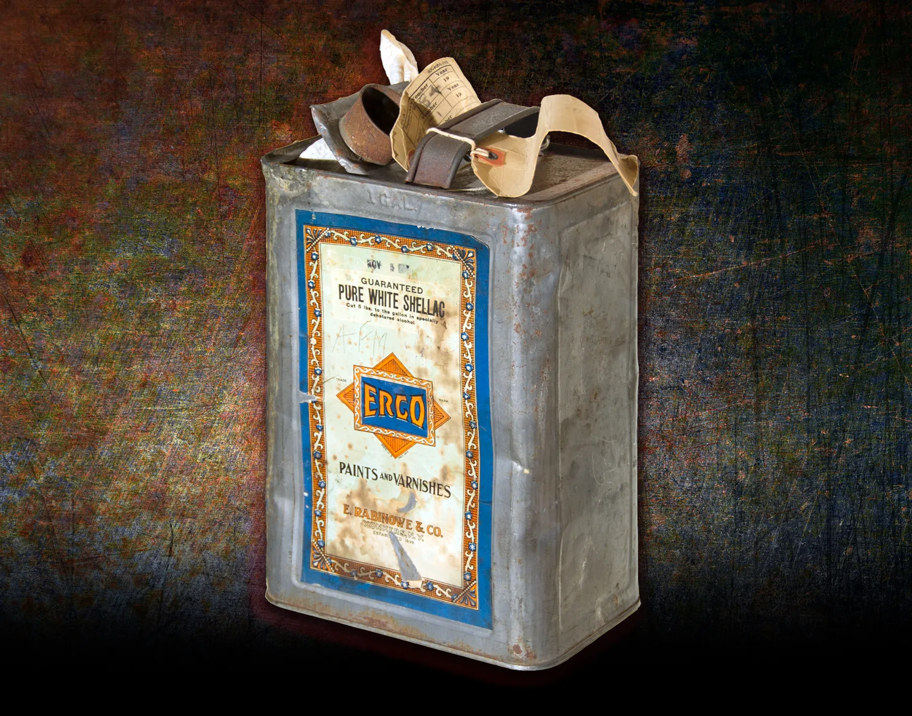 Weathered rectangular metal can with a handle, evidence tags and a shellac label, photographed against a dark background.