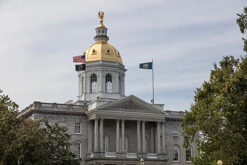 Columned New Hampshire State Capitol in Concord with a gold dome, framed by trees